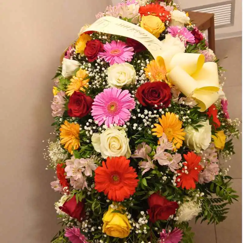 Corona funebre con rose, gerbere e nastro di condoglianze