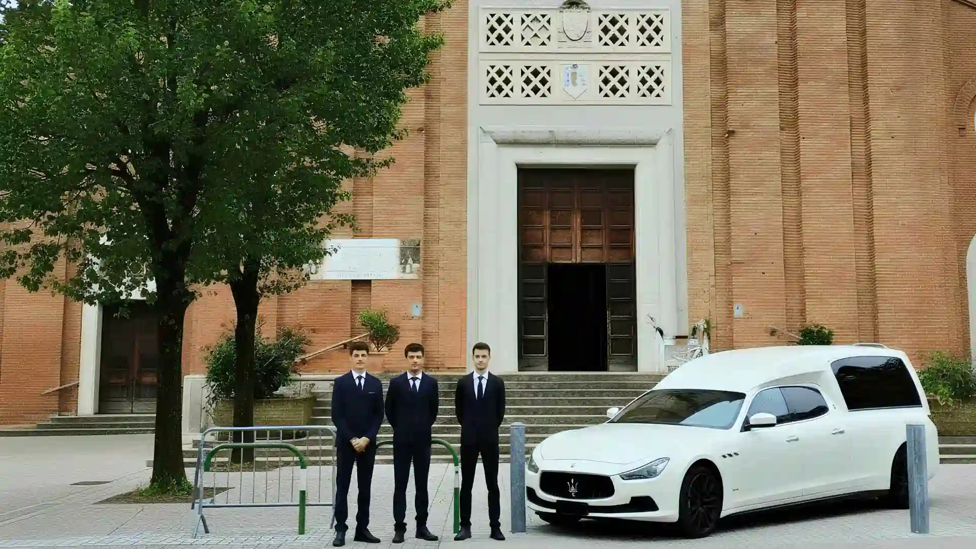 Il personale in abito scuro accanto al carro funebre davanti alla chiesa