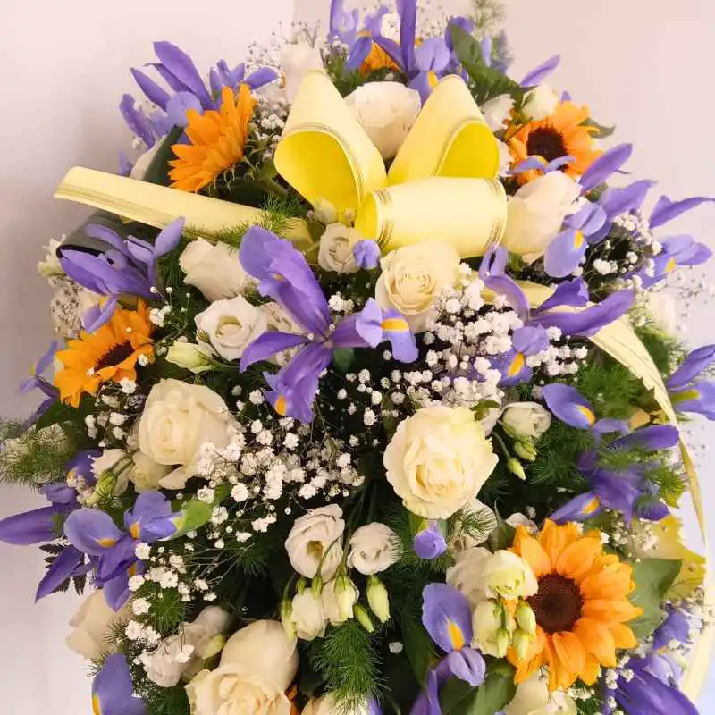 Composizione floreale con iris viola, rose bianche e girasoli con fiocco chiaro